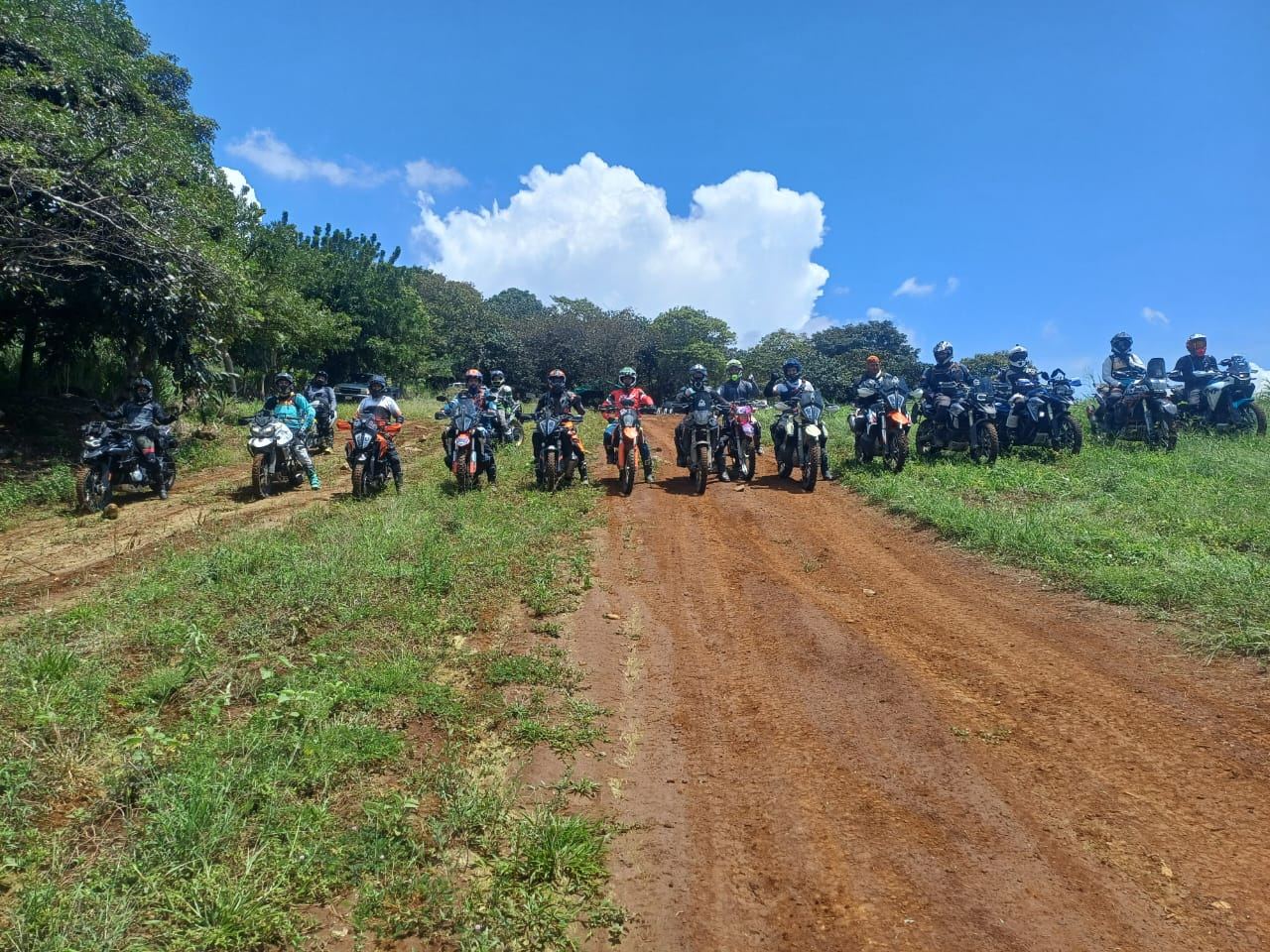 Unos quince motociclistas en fila sobre un camino de tierra roja.