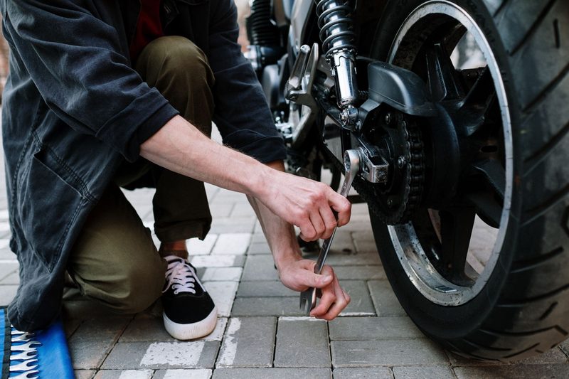 Persona agachada ajustando con una llave el eje de la rueda trasera de una moto.